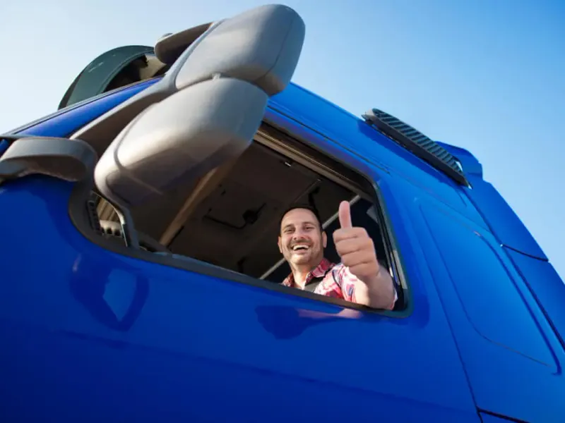 Motorista em um caminhão azul fazendo o gesto joia para a câmera 