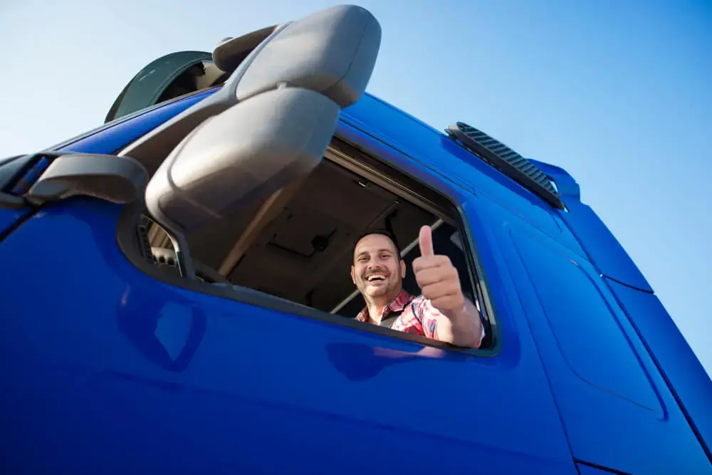 Motorista em um caminhão azul fazendo o gesto joia para a câmera